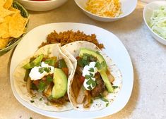 three tacos on a plate with salsa, guacamole and tortilla chips