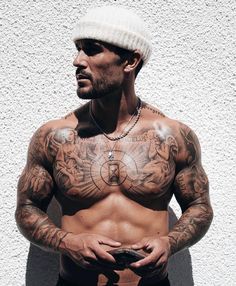 a man with tattoos on his chest holding a remote in front of a white wall