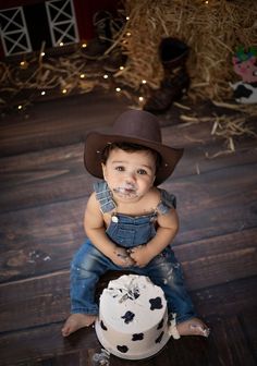 a little boy sitting on top of a wooden floor next to a cake covered in frosting