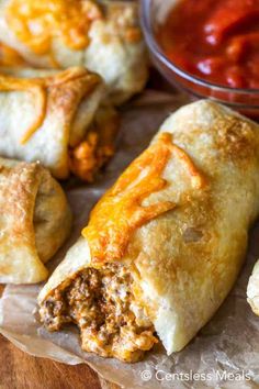 some taco stuffed pastries are sitting on wax paper with sauce in the background