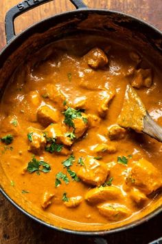 a pan filled with curry and chicken on top of a wooden table