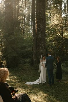 a bride and groom standing in the woods with their wedding party looking at each other