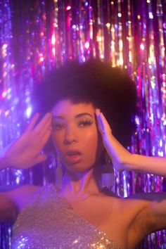 a woman in a silver dress holding her hands up to her head and looking at the camera