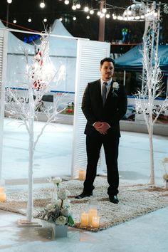 a man in a suit standing next to a white tree with candles on the ground