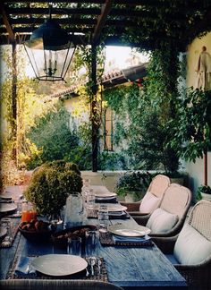 an outdoor dining area with wicker chairs and table set for four, surrounded by greenery