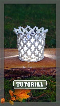 a white beaded crown sitting on top of a piece of wood next to leaves