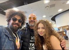 two men and a woman taking a selfie in an airport with their arms around each other