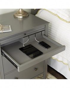 two cell phones are plugged into the charging station on a nightstand table next to a bed