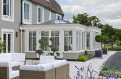 an outdoor living area with white furniture in front of a large house and lavender flowers