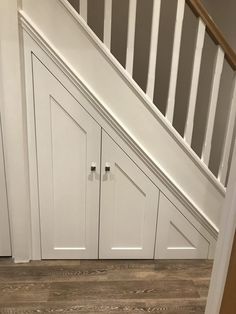 an under stair storage area with white cabinets and wood flooring on the bottom level