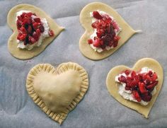 four heart shaped pastries with whipped cream and strawberries on them, sitting on a baking sheet