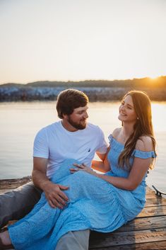 a man and woman sitting on a dock next to the water smiling at each other