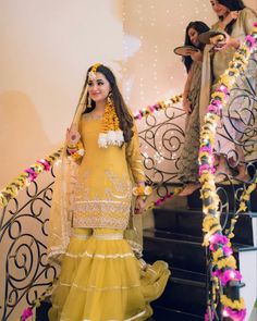 a woman in a yellow outfit standing on stairs with flowers around her neck and hands behind her head