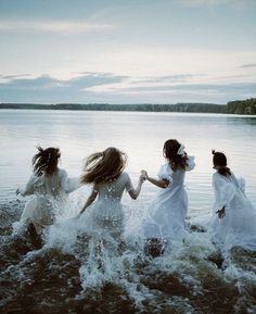 four girls in white dresses run into the water