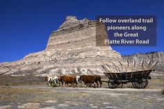 a group of horses pulling a wagon down a dirt road next to a tall mountain