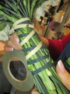 a person holding a bundle of asparagus wrapped in tape and wrapping it up