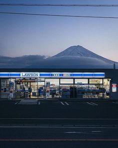 an empty parking lot in front of a building with a mountain in the background at dusk