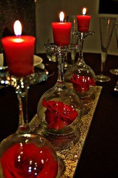 three wine glasses with red roses in them are sitting on a table next to candles