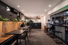 people sitting at tables in a restaurant with large windows and plants on the wall behind them