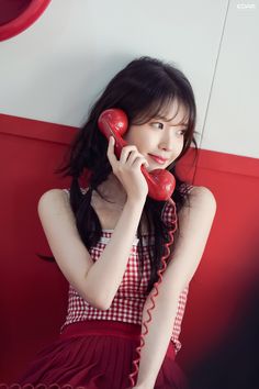 a woman in a red and white dress is talking on an old style telephone while holding her hand up to the phone