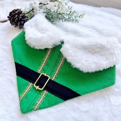 a green and black dog coat with a gold buckle on it's collar, sitting on top of a white blanket