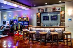 a bar with several stools in front of it and an arcade game on the wall