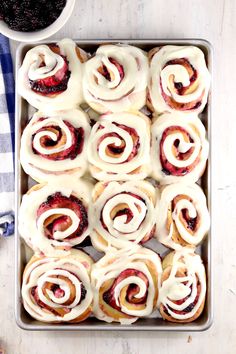 a pan filled with rolls covered in icing next to a bowl of blackberries