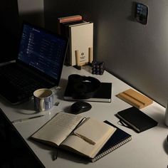 an open laptop computer sitting on top of a desk next to a cup and books