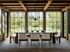 a dining room with large windows and wooden beams on the ceiling is surrounded by white chairs