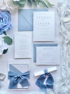 the wedding stationery is laid out with blue and white flowers, ribbons, and cards