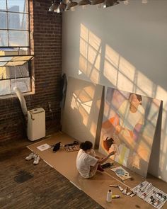 a person sitting on the floor working on paintings