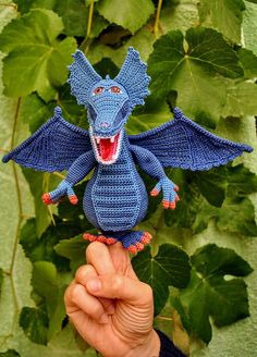 a hand holding up a knitted blue dragon