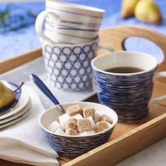 two cups of coffee and some sugar cubes on a tray with pears in the background