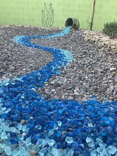 blue glass pebbles and gravel in front of a green brick wall with a water hose running through it