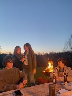 four people sitting around a fire pit at dusk