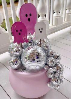 a pink vase filled with lots of shiny silver balls and ghost decorations on top of a white porch