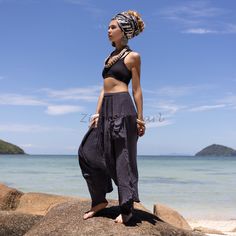 a woman standing on top of a rock next to the ocean and wearing a head scarf