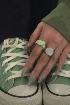 a woman's hand with green and white nail polish holding onto an apple ring