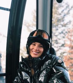 a woman in a black jacket and goggles is sitting on a ski lift smiling at the camera