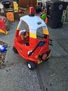 a small toy fire truck sitting on top of a cement floor next to trash cans