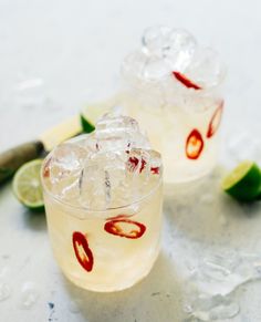 two glasses filled with ice and limes sitting on top of a white countertop