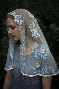 a woman wearing a veil with blue flowers on it and a head piece in front of her face