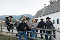 a group of men standing next to each other near a wooden fence in front of a barn