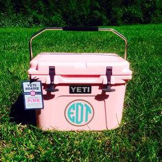 a pink yeti cooler sitting in the grass with a sticker on it's side