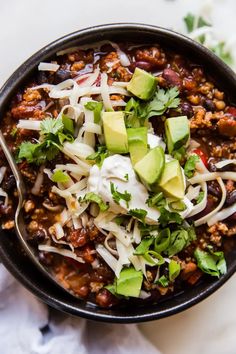 a bowl filled with chili, cheese and avocado on top of a table