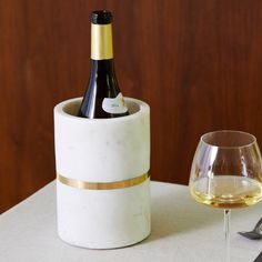 a bottle of wine in a marble holder next to a glass on a white table