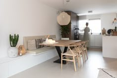 a person is standing in the kitchen behind a table with chairs and a bench on it