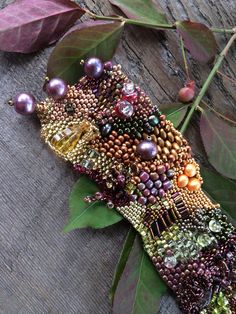 a piece of art made out of beads and other items on a wooden surface next to leaves