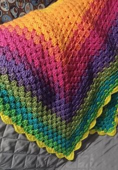 a multicolored crocheted blanket sitting on top of a bed next to a pillow