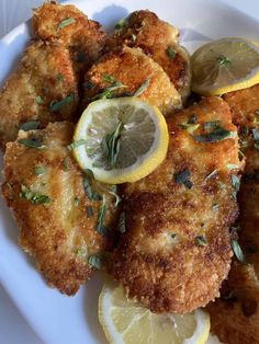 fried chicken with lemon slices and herbs on a white plate